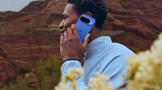 A man holds a blue phone to his ear while standing in a rocky landscape.